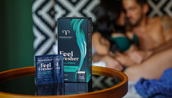 Promescent before and after wipes on a glass table with a blurred out couple engaged in foreplay in the background