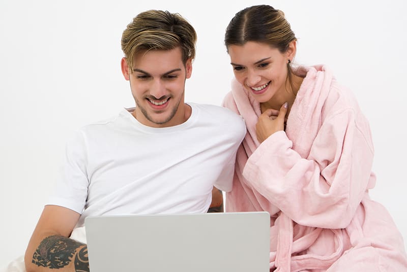 Couple sitting on bed reviewing health tips for daily sex online