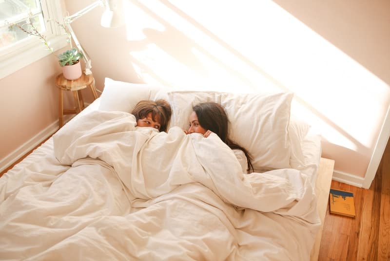 Two women laying in bed excited about scissoring